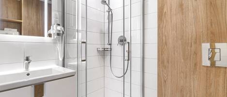 Un baño moderno con ducha envuelta en vidrio, un lavabo blanco y una pared de acento de madera.