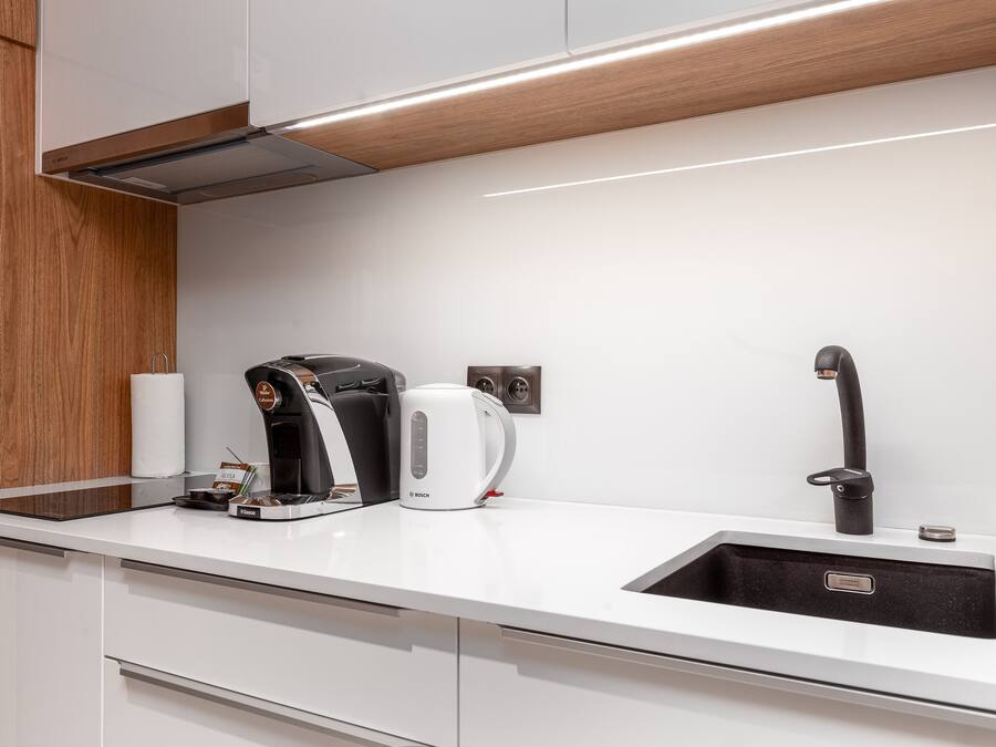 A modern kitchen with a white countertop, a Bosch coffee maker, a kettle, and a sink.