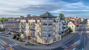 A multi-story building with a corner entrance, a pedestrian crossing, and a street view with cars and pedestrians. - City Apartments - Apartamenty Młyńska 49 (Koszalin)