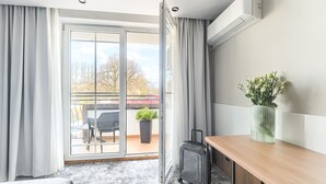 A hotel room with a sliding glass door to a balcony, a small table with a vase of flowers, and a suitcase on the floor. - City Apartments - Apartamenty Młyńska 49 (Koszalin)