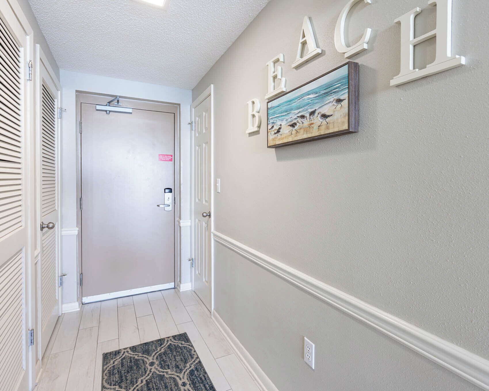 A hallway with a beige wall, a framed painting of birds on the wall, and a door with a lock.