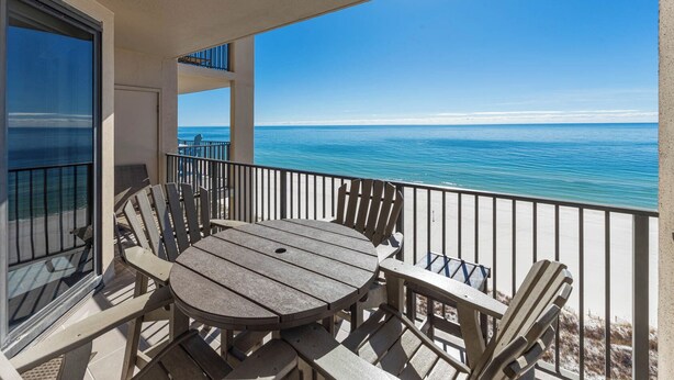 Ein Balkon mit Holztisch und Stühlen, der auf einen Strand und das Meer blickt.