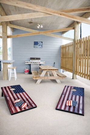 An outdoor patio with a wooden table and benches, a barbecue grill, and a flag on the wall. - Private Pool | Pet-Friendly | Beach Access (Gulf Shores)