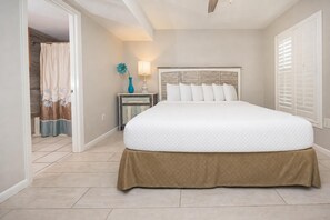A bedroom with a large bed, a nightstand with a lamp, and a view of the bathroom. - Phoenix I Condo 1084 ~ One Bedroom (Orange Beach)