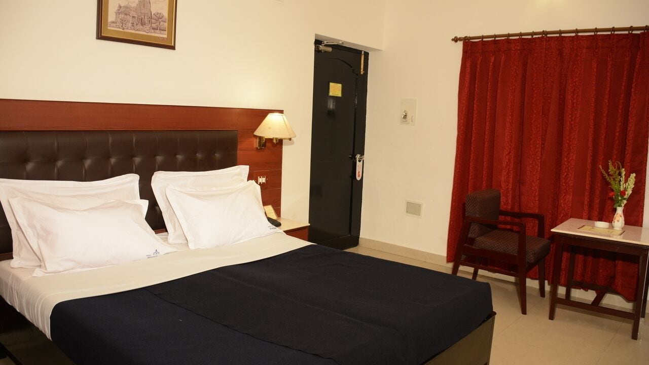 Hotelkamer met een bed, een bureau, een stoel, een deur en een rood gordijn.