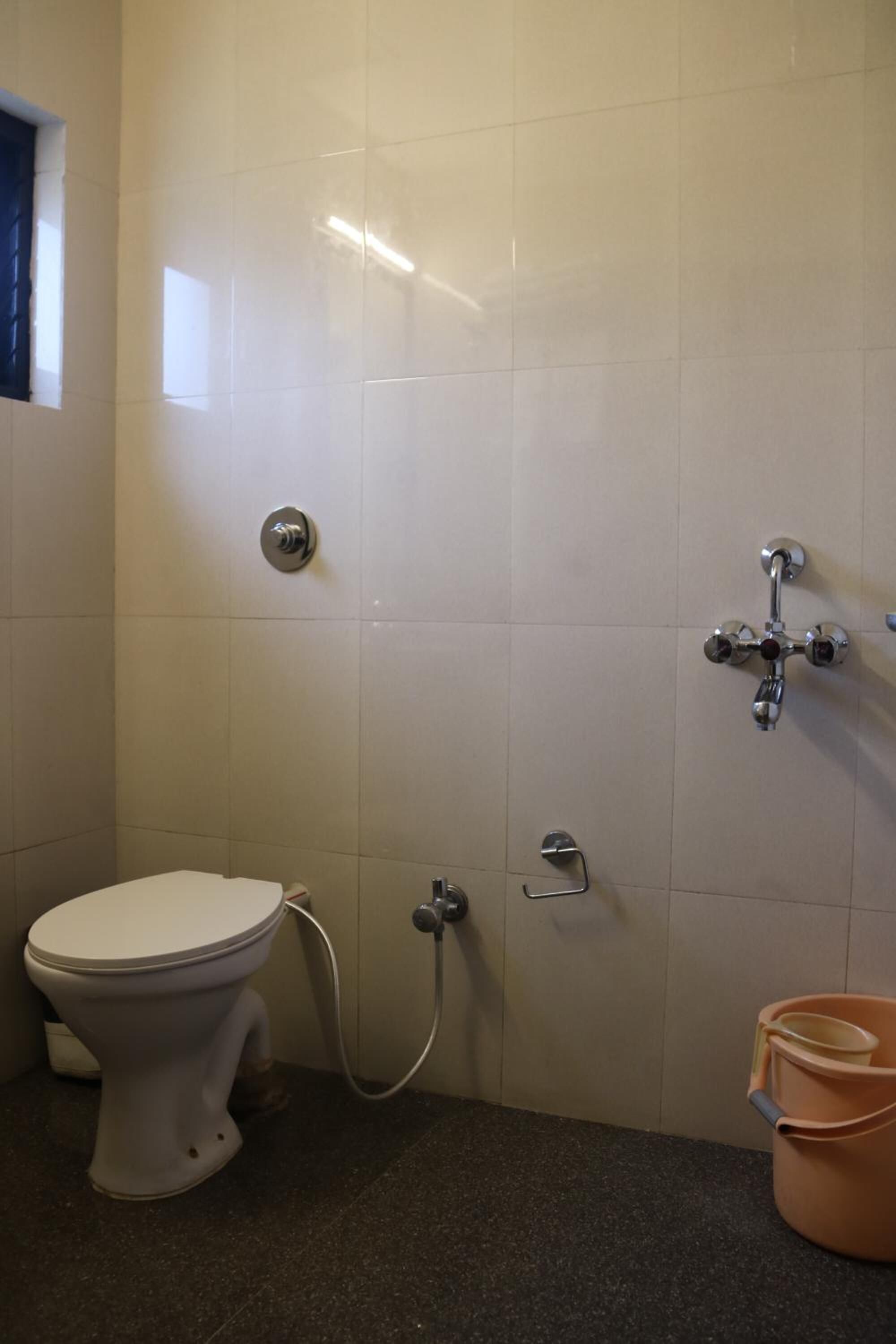 A bathroom with a toilet, a shower, and a bucket.