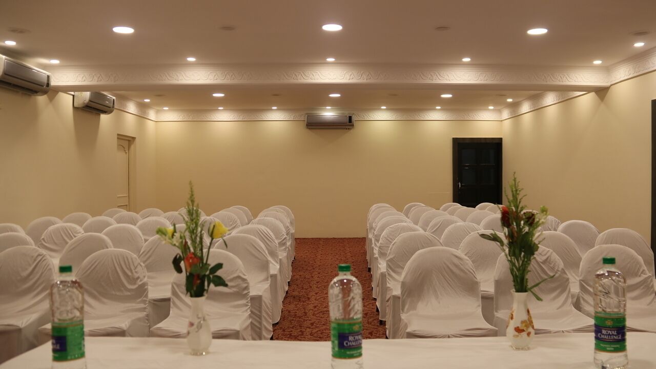A conference room with rows of white-covered chairs, tables with water bottles and vases, and a carpeted floor.