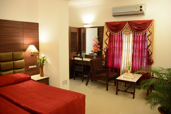 Habitación de hotel con cama, escritorio, silla, mesa, lámpara y planta en maceta.