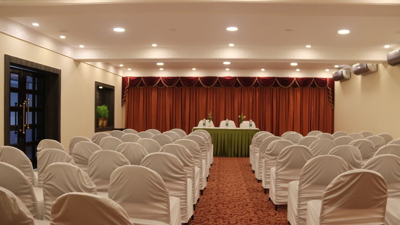 A conference room with rows of chairs, a stage with a green table, and red curtains.