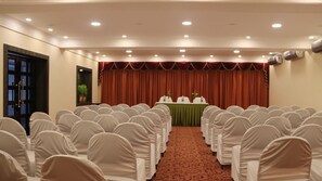 A conference room with rows of chairs, a stage with a green table, and red curtains. - Hotel Grand central (Bhubaneshwar)