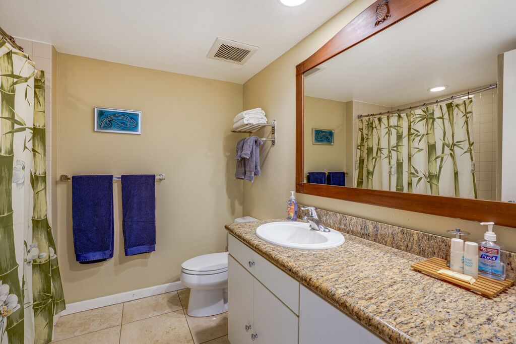 Une salle de bain avec un lavabo blanc, un miroir et des toilettes. Des serviettes sont accrochées au mur et il y a un rideau de douche à motifs de bambou.