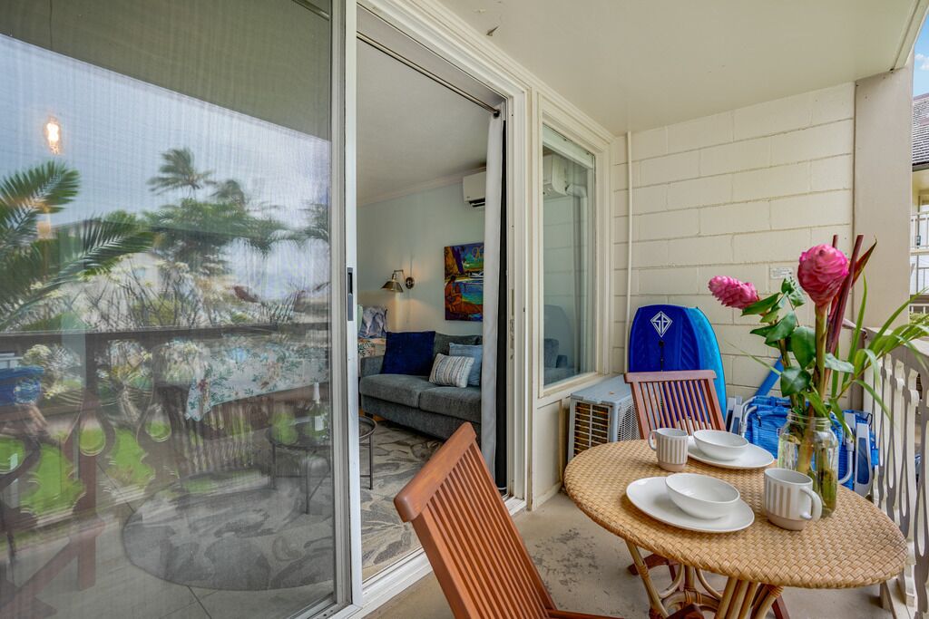 A balcony with a dining table, chairs, and a vase with flowers.
