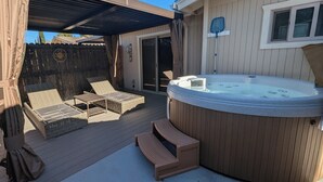 Un patio trasero con un jacuzzi, sillones de descanso y un porche cubierto.