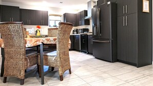 Una cocina moderna con armarios oscuros, un refrigerador de acero inoxidable y un comedor con sillas de mimbre y una mesa de mármol.
