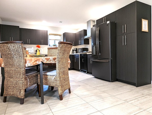 A modern kitchen with dark cabinetry, a stainless steel refrigerator, and a dining area with wicker chairs and a marble table. - CENTRALLY LOCATED Zen Hideaway: Private Hot Tub & Walk to Trails! (Sedona)