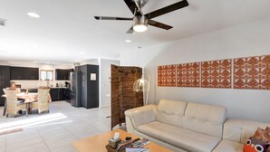 Una sala de estar moderna con un sofá, una mesa de centro con revistas, un ventilador de techo y una cocina al fondo.