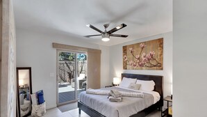 Un dormitorio con cama, mesitas de noche, ventilador de techo y una puerta corrediza de vidrio que da a un espacio al aire libre.