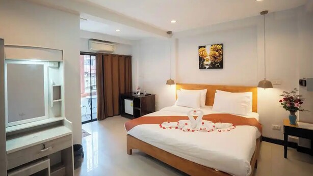 Quarto de hotel com cama, escrivaninha, cadeira, televisão, janela com cortinas e uma obra de arte na parede.