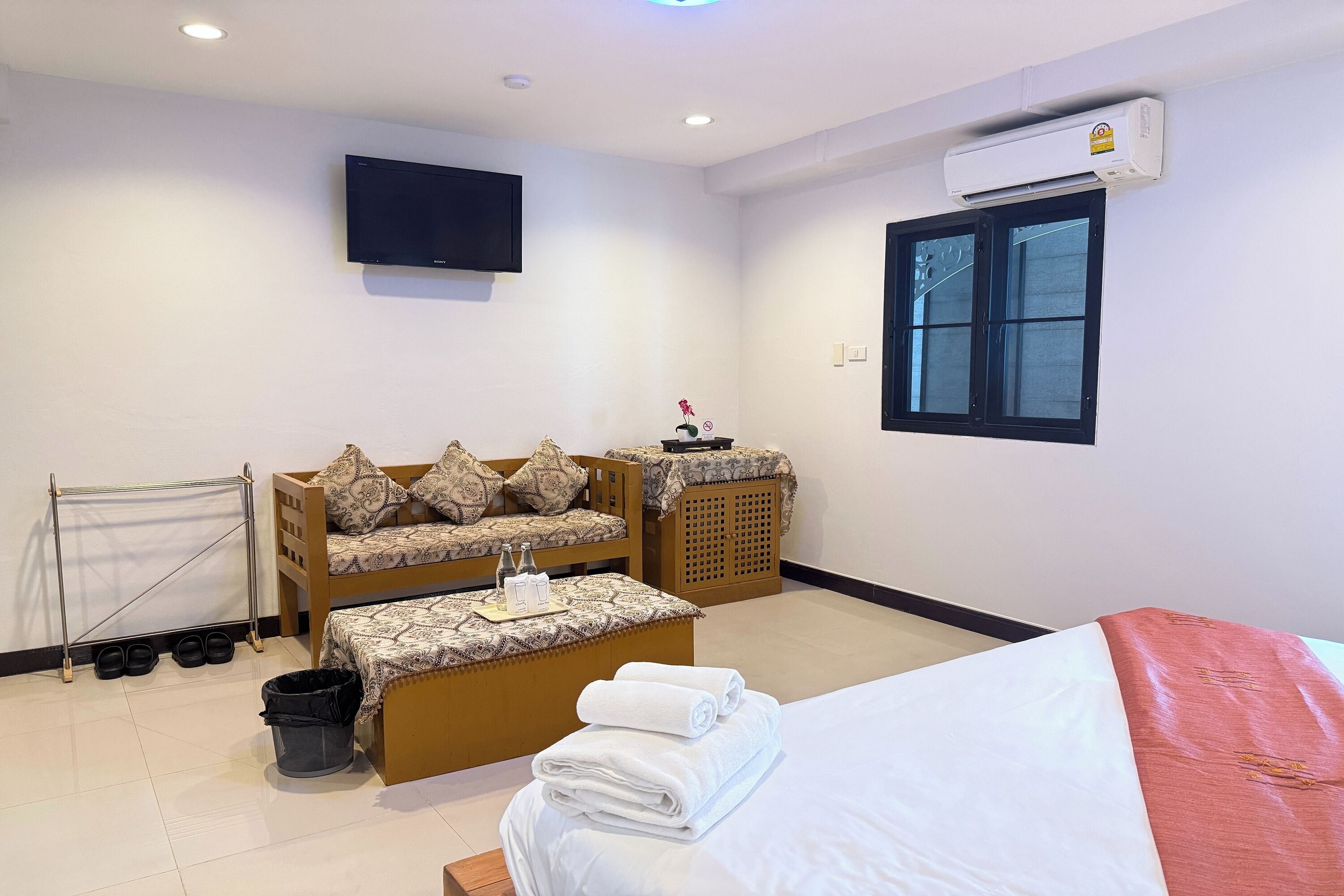 Een hotelkamer met een bed, een bank, een televisie, een airconditioner en een raam.