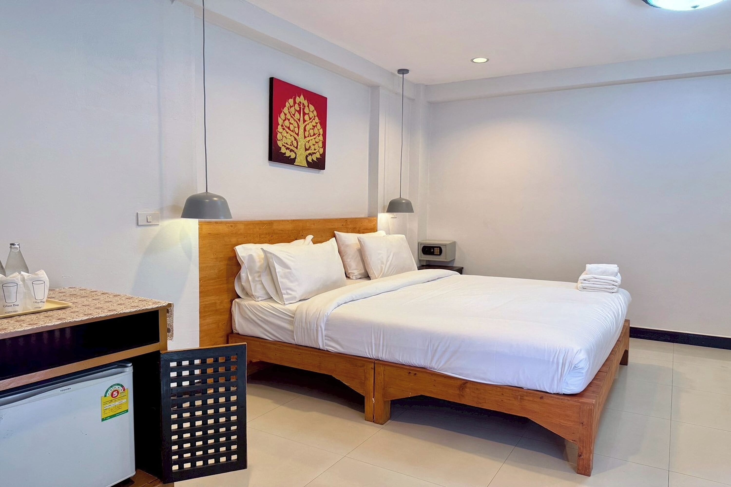 A neatly arranged hotel room with a wooden bed, white bedding, a small desk with a lamp, and a refrigerator.