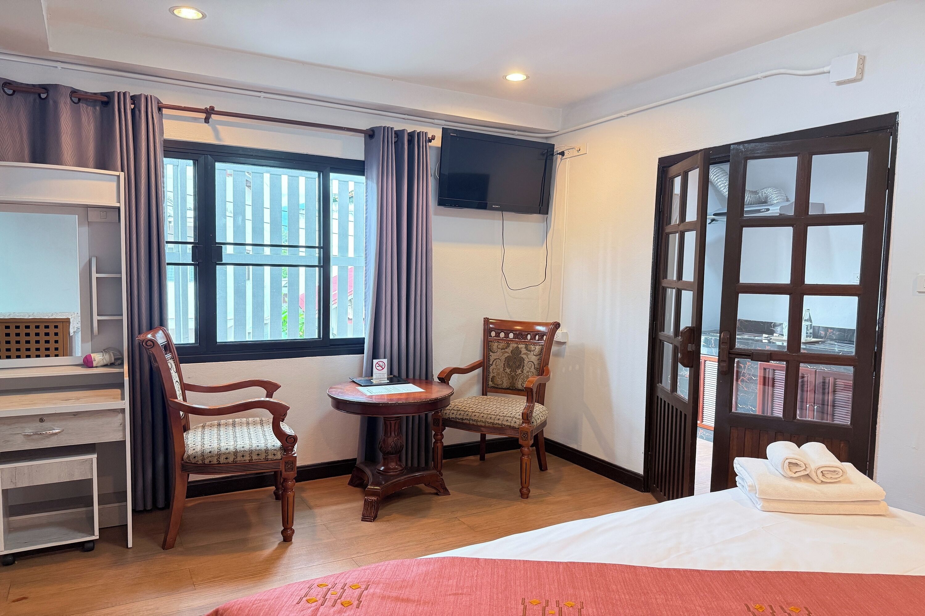 A hotel room with a bed, a desk, a chair, a TV mounted on the wall, and a window with curtains.
