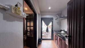 Um corredor estreito com piso de madeira, uma área de cozinha com bancada e armários pretos, e vista para um pátio externo por uma porta de vidro.