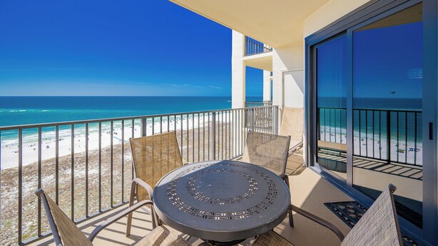 A balcony with a round table and chairs, overlooking a beach with clear blue water and a sandy shore. - Phoenix VII 71414 Gulf-Front Orange Beach Condo (Orange Beach)