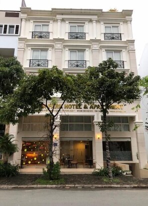 Un hôtel à la façade classique, doté d’une grande entrée avec une porte en verre et d’un espace extérieur aménagé avec des sièges.