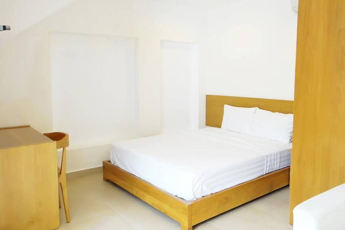 Ein schlicht eingerichtetes Schlafzimmer mit einem Holzbett, einem kleinen Holztisch und einer schlichten weißen Wand.