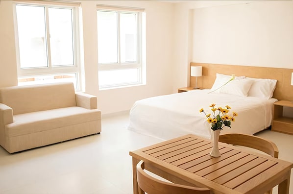 Una habitación de hotel con cama, sofá, una mesa de madera y un jarrón con flores.
