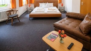 A hotel room with a bed, a sofa, a TV, and a small table with a vase of flowers. - Hotel Waldmühle (Oberharz am Brocken)