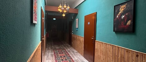 Un pasillo con paredes color turquesa, alfombra estampada, paneles de madera y un candelabro.