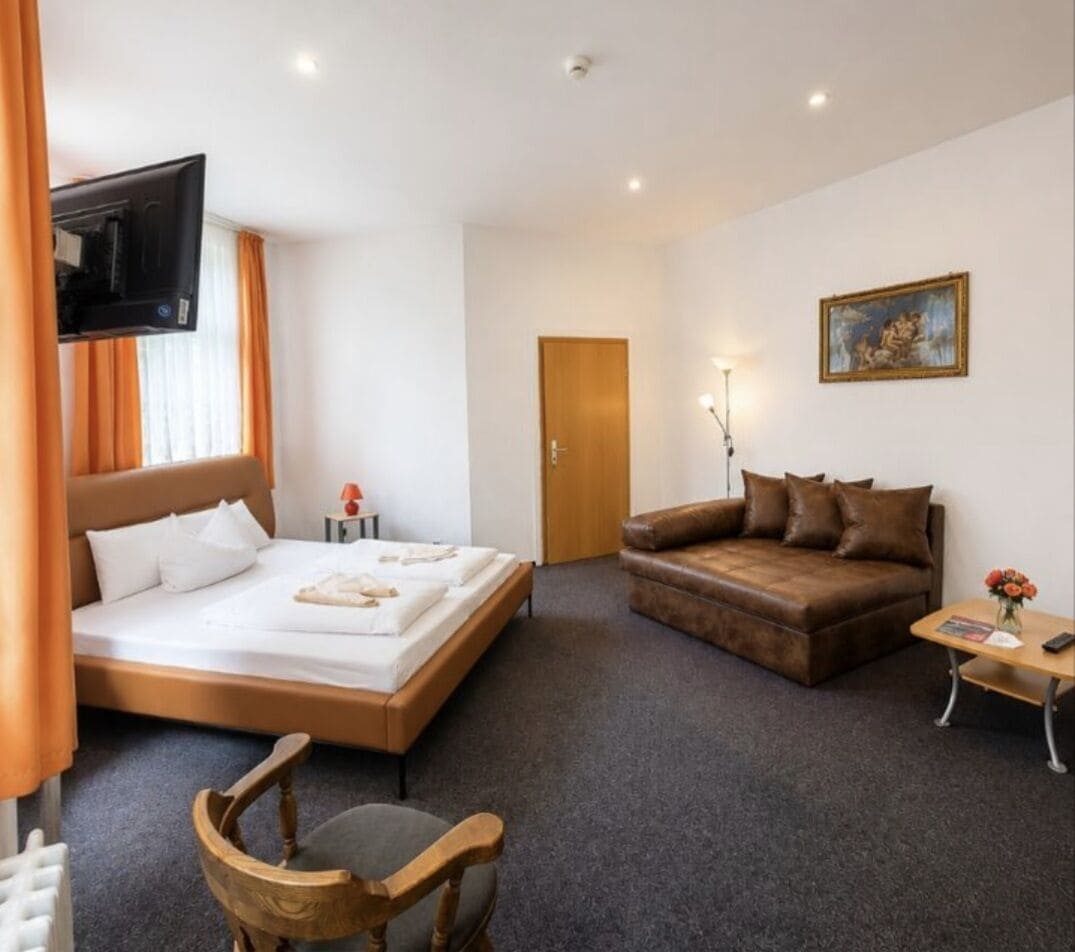 Ein Hotelzimmer mit einem Bett, einer Couch, einem Fernseher, einem Gemälde und einer Tür.