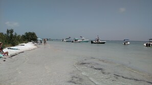 Uma praia com barcos ancorados perto e pessoas relaxando na areia.