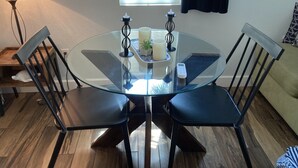 Une table ronde en verre, quatre chaises noires, une bougie, une télécommande et une petite plante.