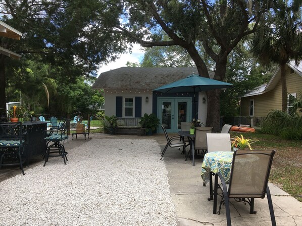 An outdoor patio area with tables and chairs, a covered seating area, and a building with a blue door and windows.