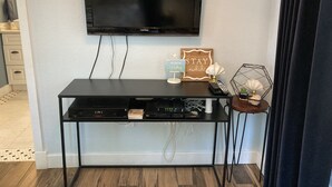 Un téléviseur à écran plat est fixé au mur, au-dessus d’un meuble noir contenant des appareils électroniques, et une pancarte indique : « RESTEZ ici pendant que vous travaillez. »