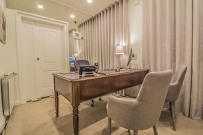 A hotel room with a wooden desk, two chairs, a lamp, a computer, and a window with curtains.