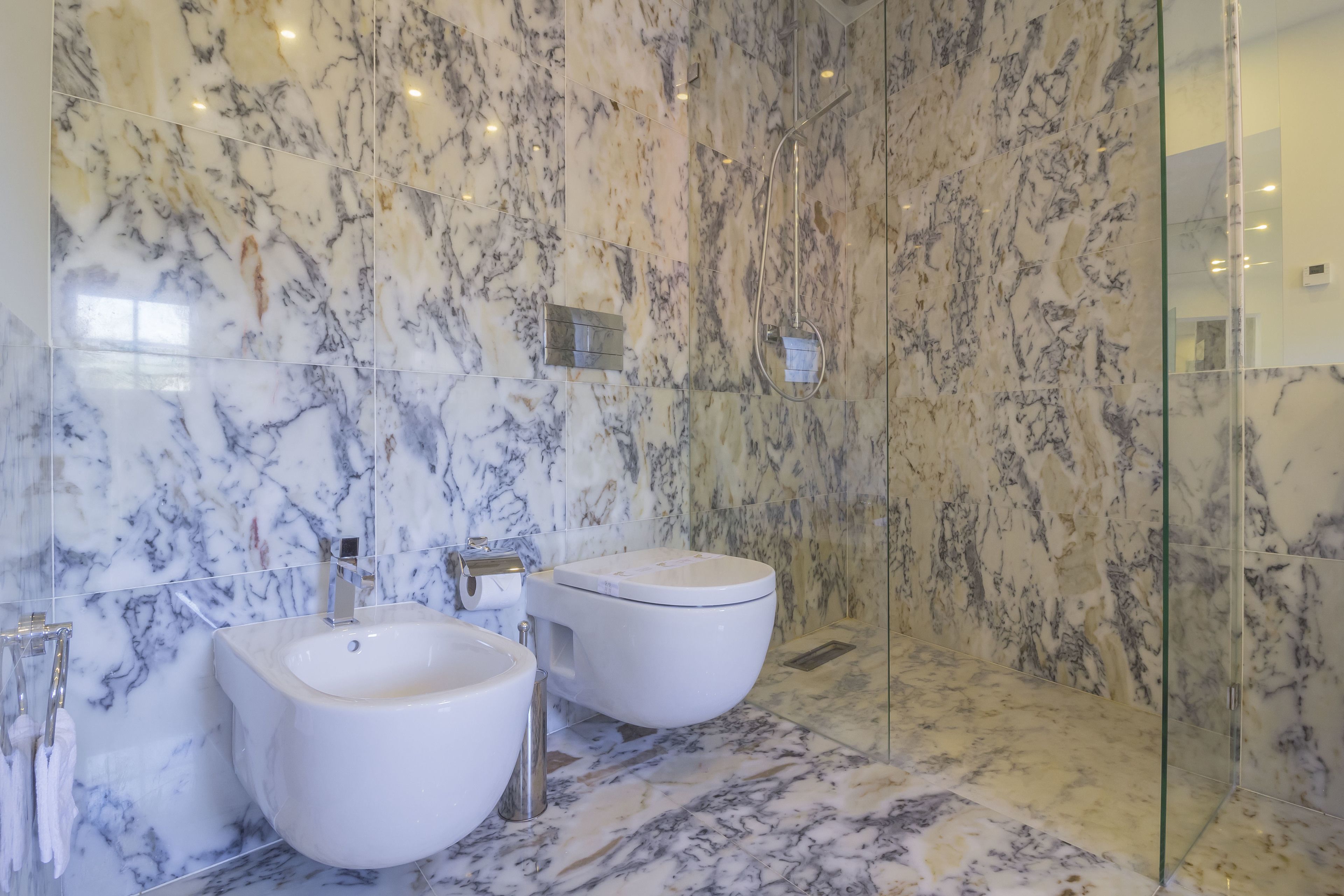 A bathroom with marble walls and floor, a glass shower enclosure, and two sinks.