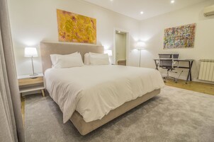 Un dormitorio con una cama grande, dos mesitas de noche, un escritorio con silla y dos lámparas de pared.