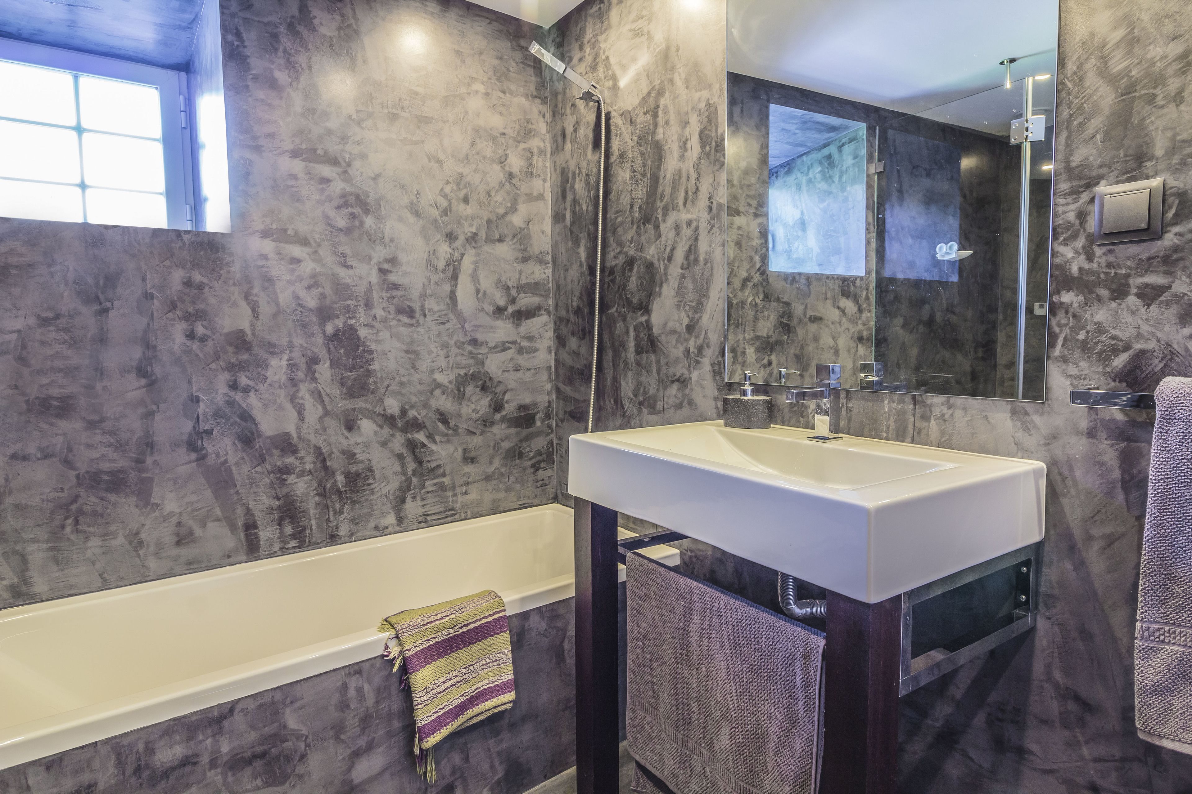 A modern bathroom with a marble wall, a bathtub, a sink, and a mirror.