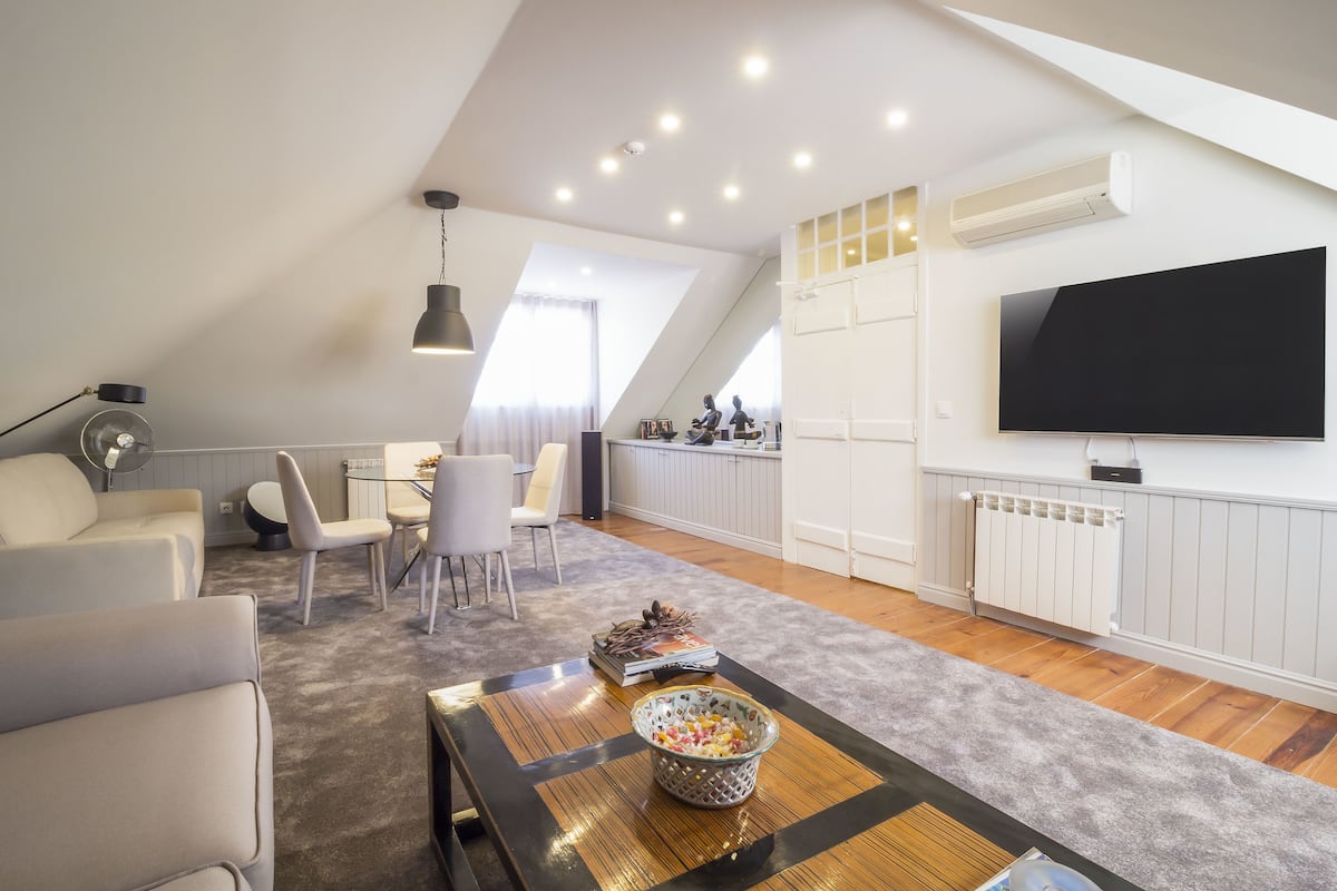 Een moderne woonkamer met een grote flatscreen televisie, een eethoek met stoelen, een bank en een salontafel met decoratieve objecten.