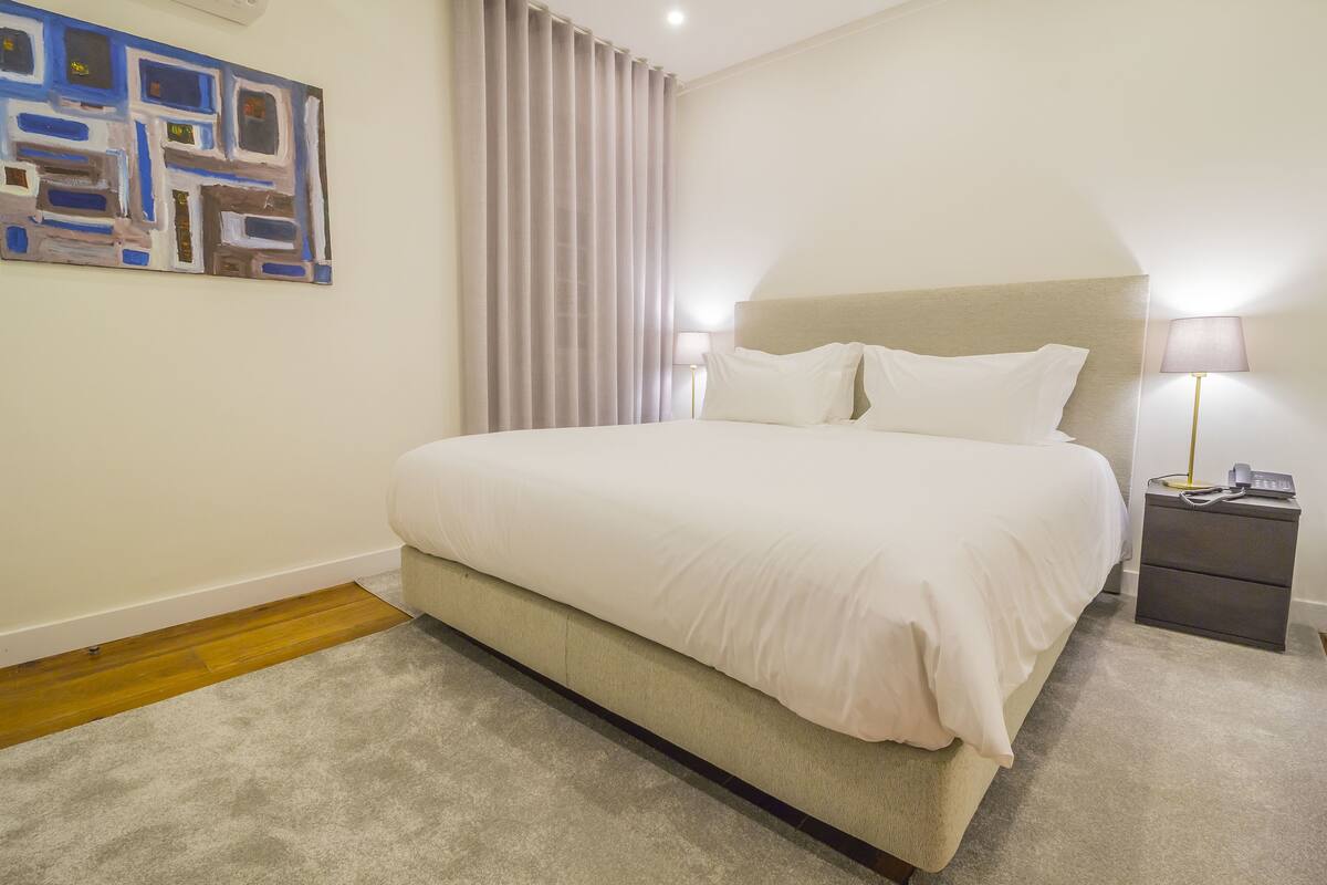 Een netjes ingerichte hotelkamer met een groot bed, een nachtkastje met een lamp en een schilderij aan de muur.