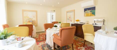 A hotel dining area with round tables, chairs, and a patterned carpet.