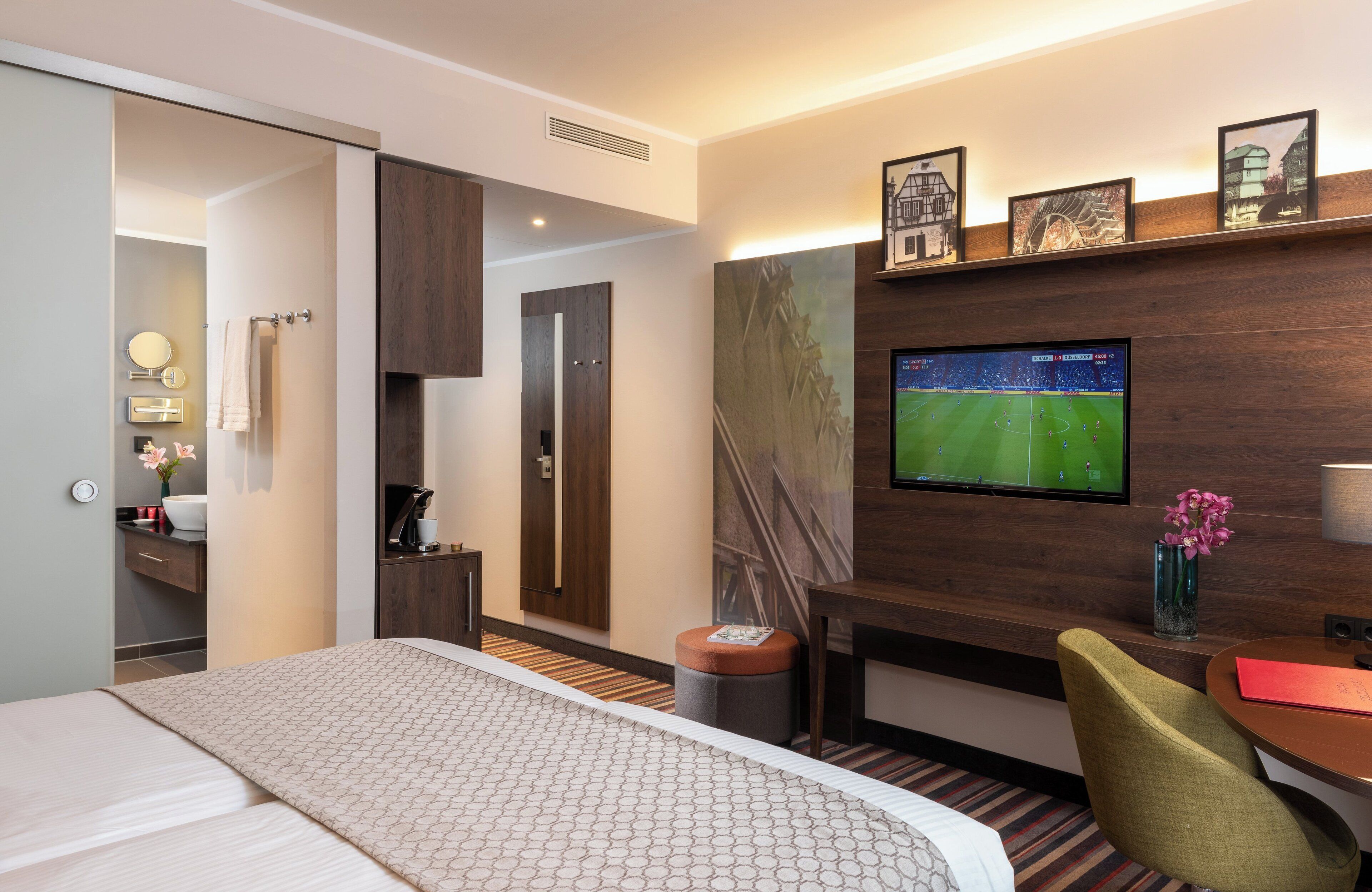 Ein Hotelzimmer mit Bett, Schreibtisch, Stuhl, Fernseher und einem durchgegangenen Tür sichtbaren Badezimmer.