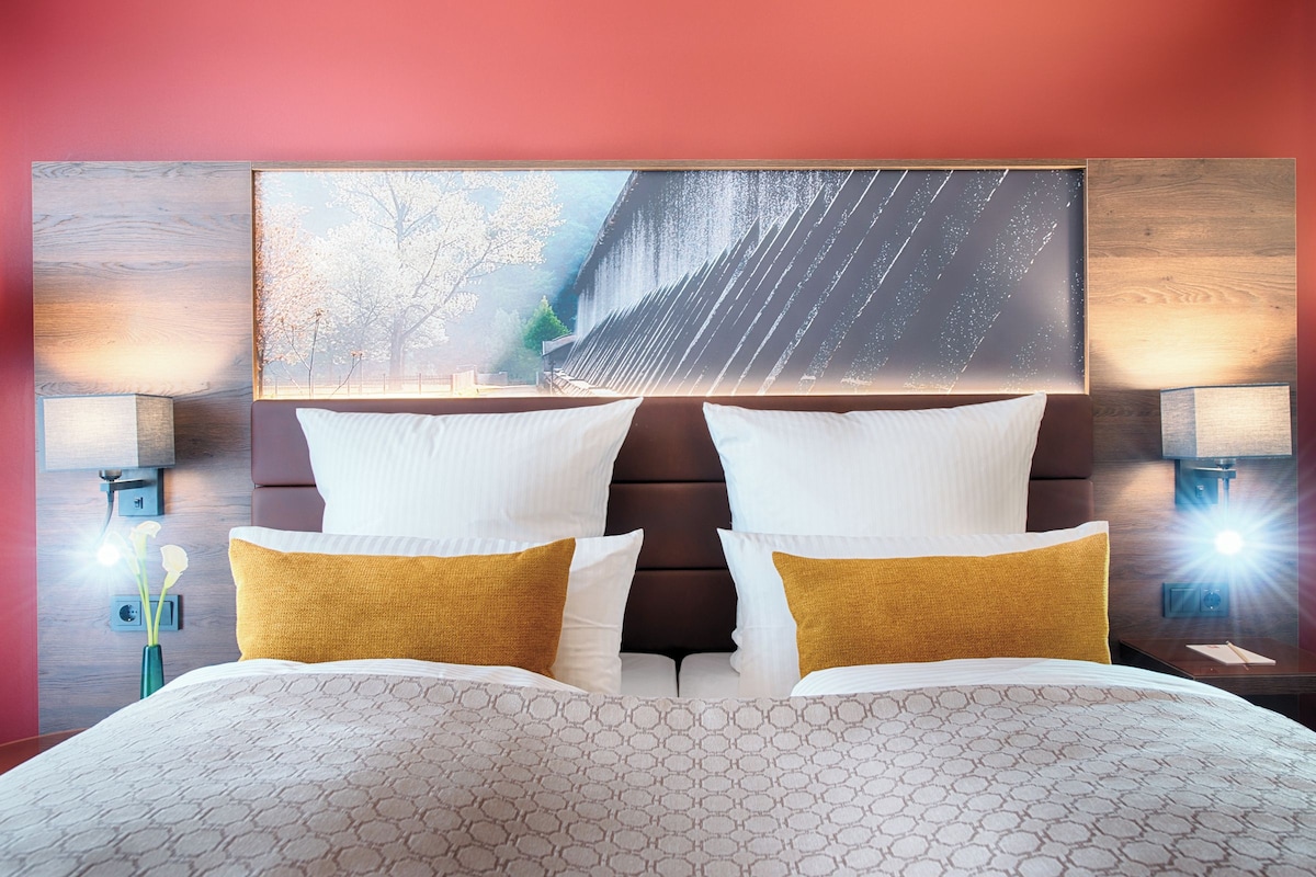 A hotel room with a large bed, two bedside lamps, a nightstand, and a wall-mounted artwork.