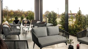 Un espacio moderno de estar al aire libre con mobiliario de mimbre y vistas a un jardín ajardinado.