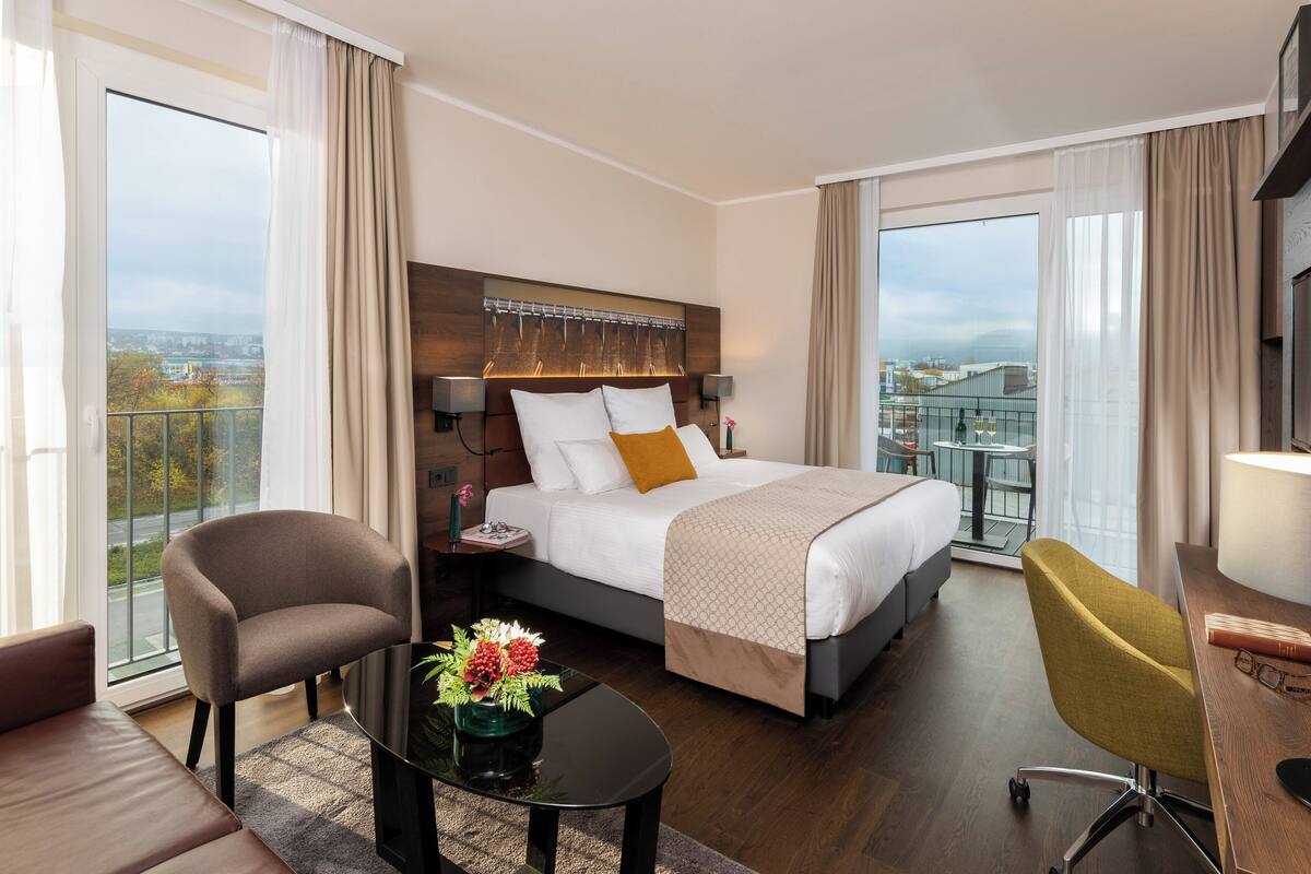 A hotel room with a large bed, a desk, a chair, and a view of the city.