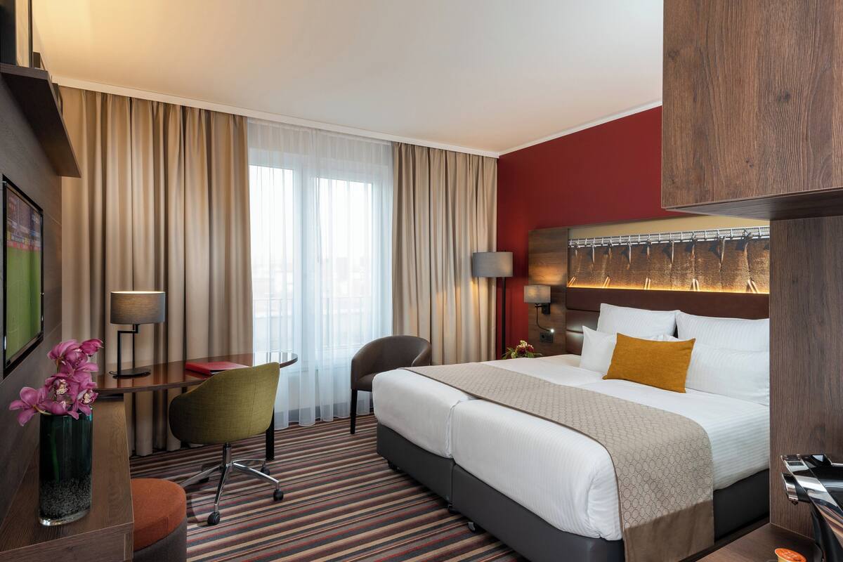 A hotel room with a large bed, a desk with a chair, a small table, and a TV.