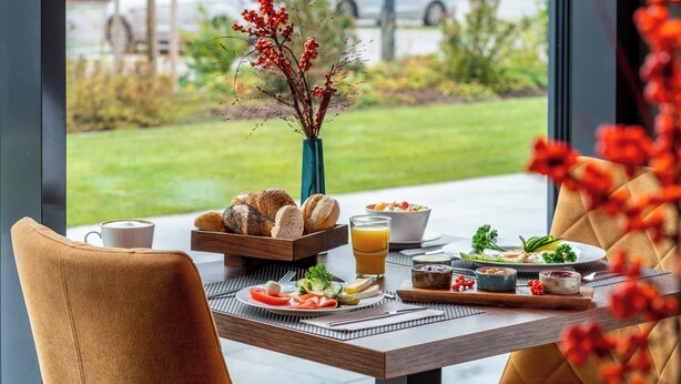 Una mesa de desayuno con diversos alimentos, una taza de café y un florero con bayas rojas.